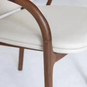 Close-up of a chair with a smooth, curved wooden frame and a cushioned seat upholstered in light beige material. The design looks modern and minimalistic.