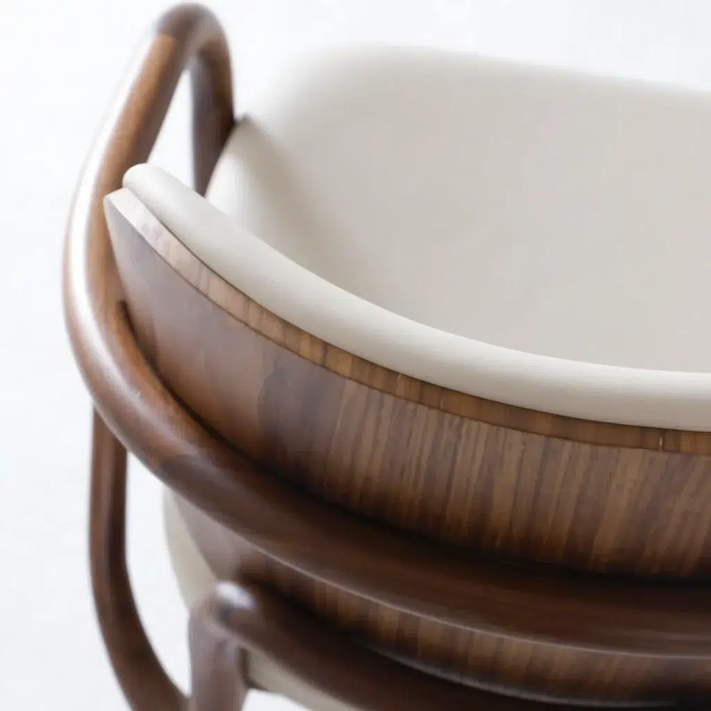 Close-up of a modern chair with a curved wooden frame and a light beige cushioned seat and backrest, set against a plain white background.