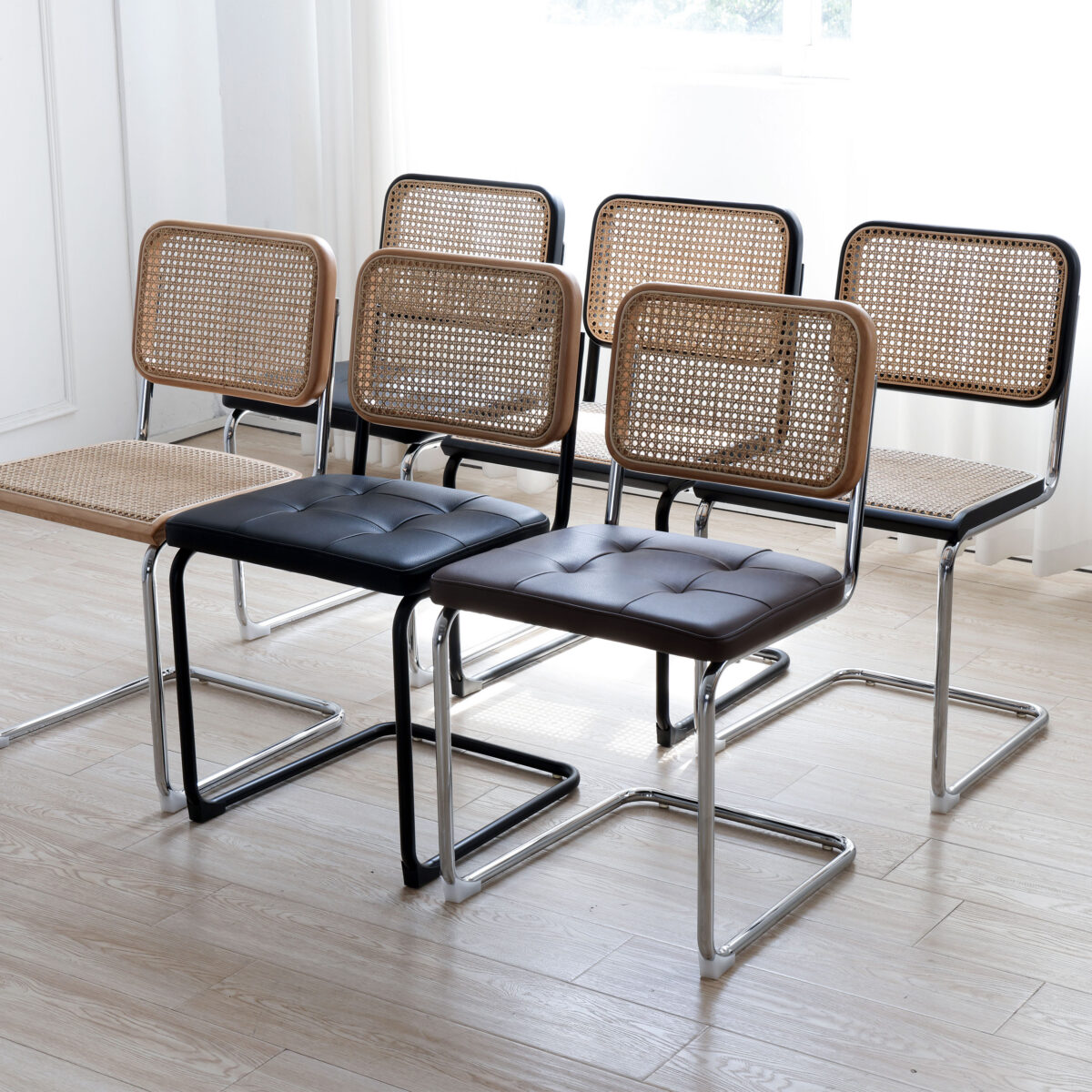 Natural Frame_Black Metal_Black Leather_C2 Six modern chairs with metal frames arranged in two rows. Four chairs have woven rattan seats and backs, while two in the front row have black cushioned seats and matching rattan backs. The floor is light wood.