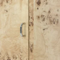 Close-up of a wooden cupboard with a shiny silver handle. The wood has a light, natural colour with unique swirling grain patterns and small knot clusters.