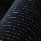 Close-up of dark fabric with diagonal white dashed lines forming a striped pattern. A seam runs vertically through the centre, highlighting the texture and stitching detail.
