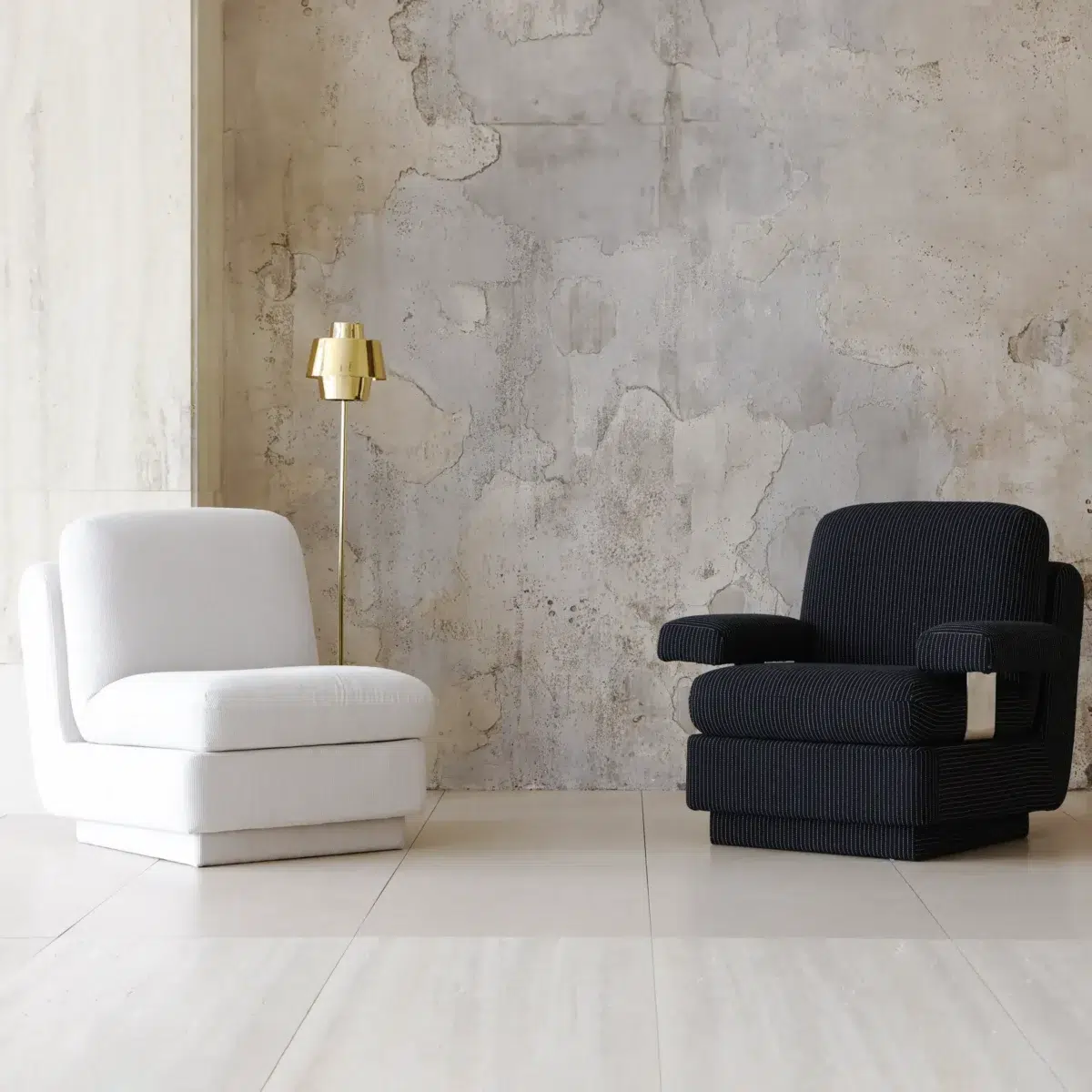 Rest Sofa_Black_Pair_Front Side View(2) A modern minimalist room with a white armless chair, a black armchair with white detail, and a gold floor lamp. The background features a textured concrete wall and light-coloured tiled floor.