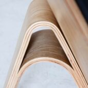 Close-up of a piece of bent plywood furniture, showing smooth, curved layers and a triangular arch design with a natural wood finish.