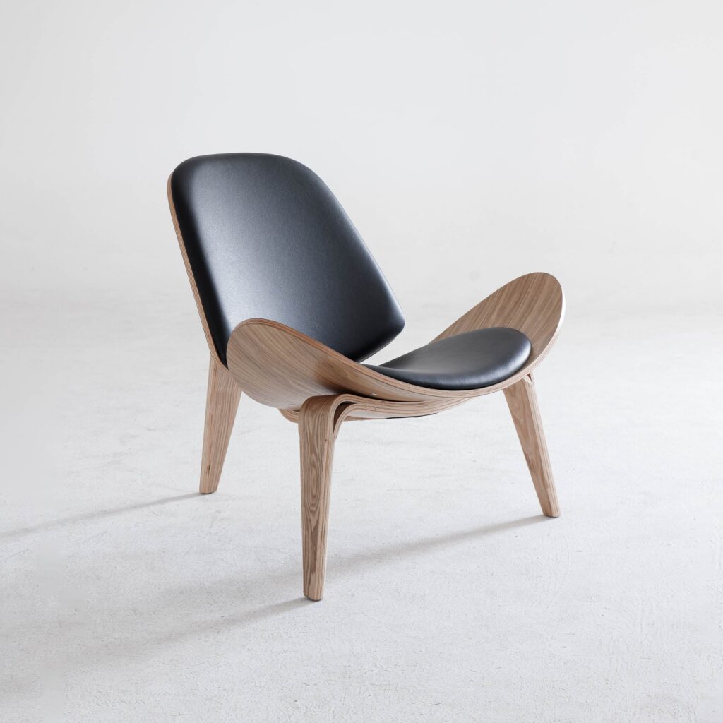 A modern chair with light wooden legs and frame, featuring a curved design and black leather seat and backrest, positioned on a plain white background.