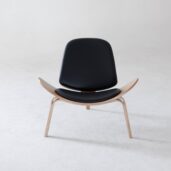A modern lounge chair with a curved wooden frame and black leather seat and backrest, placed on a smooth, light grey floor against a plain white background.