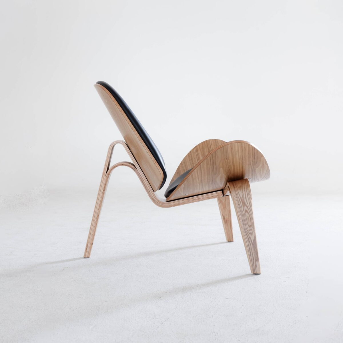 Shell Chair_Natural_B7 A modern wooden lounge chair with a sleek, sculptural design and black upholstered seat, set against a plain white background.