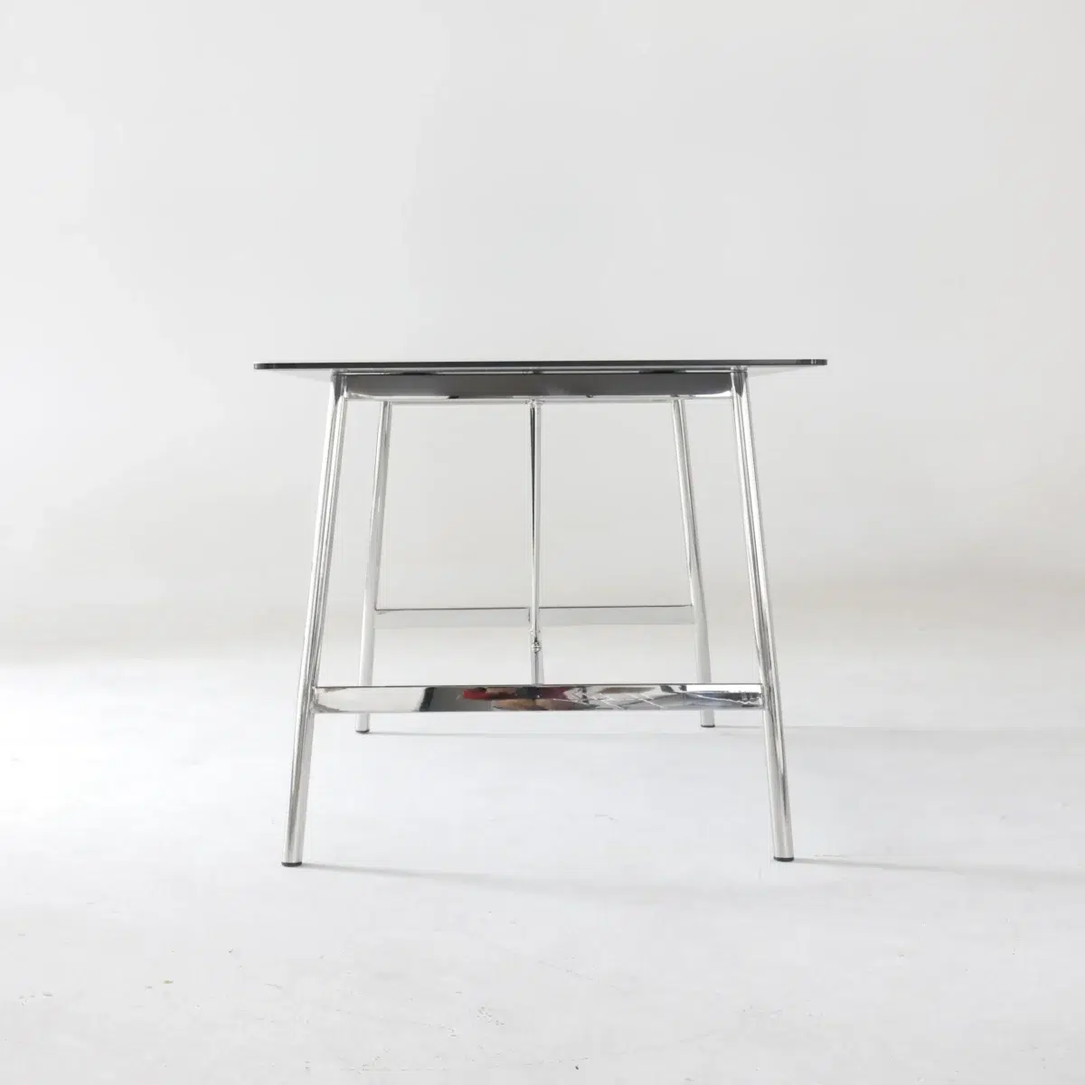 Shuge Dining Table_Side View_Clean Background A minimalist table with a black rectangular top and thin, chrome metal legs, set against a plain white background.