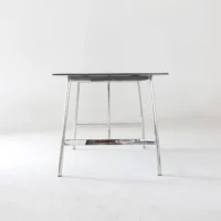 A minimalist table with a black rectangular top and thin, chrome metal legs, set against a plain white background.