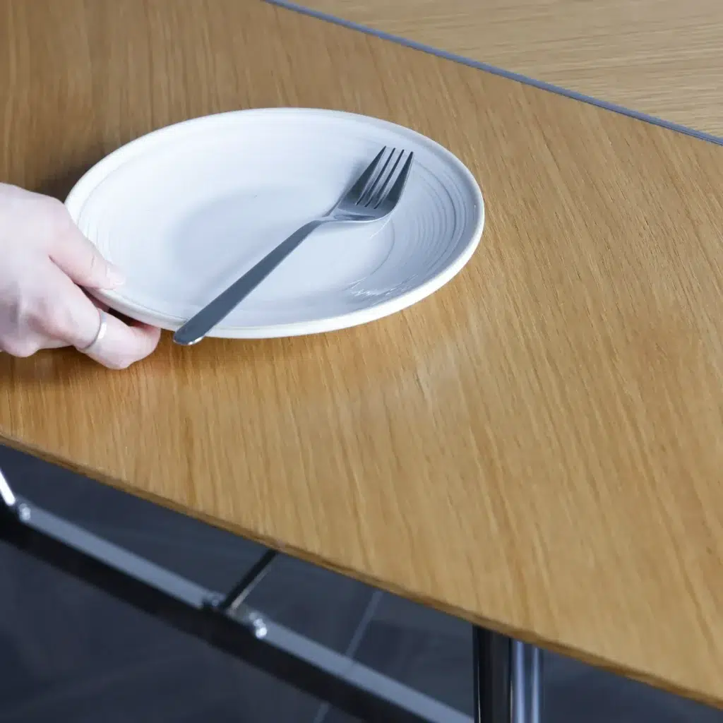 A hand places a white ceramic plate with a fork on a wooden table.