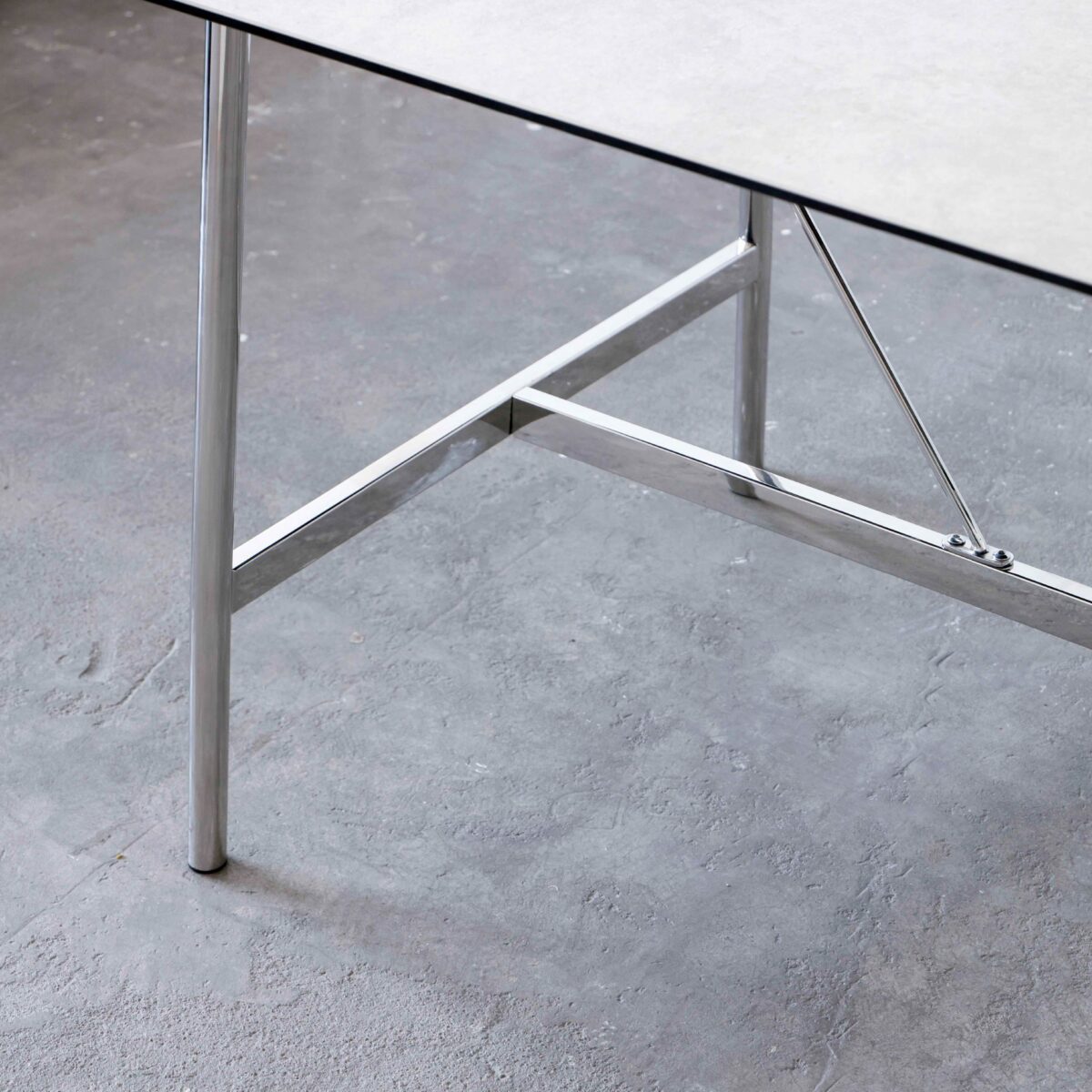 Shuge Dining Table_White_B5 A close-up view of a table with a grey tabletop and shiny metal legs, set on a textured grey concrete floor.