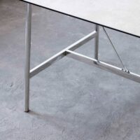 A close-up view of a table with a grey tabletop and shiny metal legs, set on a textured grey concrete floor.