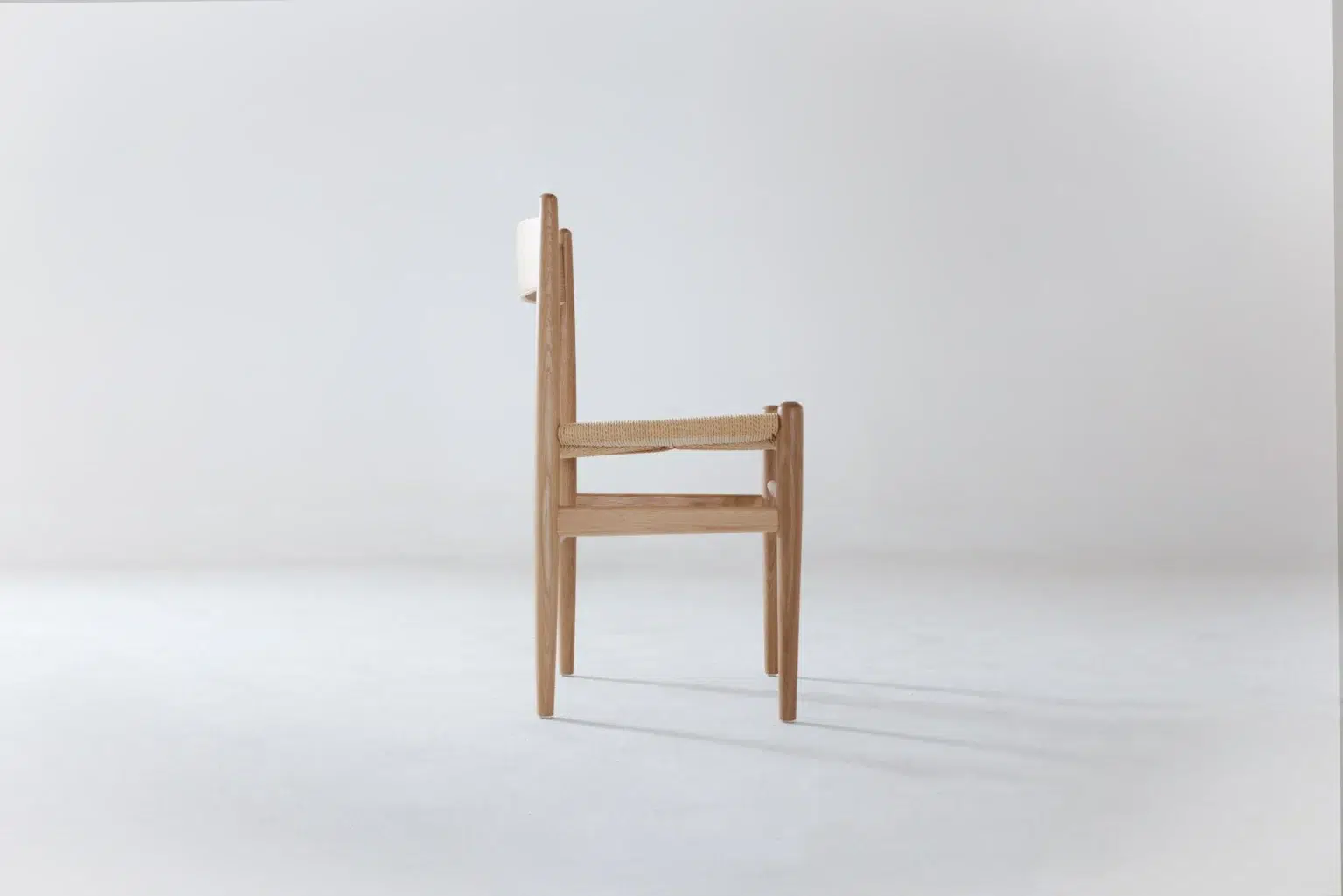 Side view A minimalist wooden chair with a natural woven seat and a simple, straight backrest, shown in profile against a plain white background.