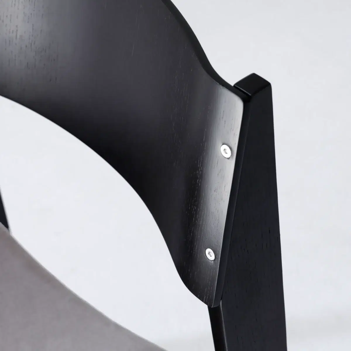 Walk Slowly Chair_Black_Detail(4) Close-up of the backrest and frame of a modern black wooden chair with visible screws, set against a plain light background.