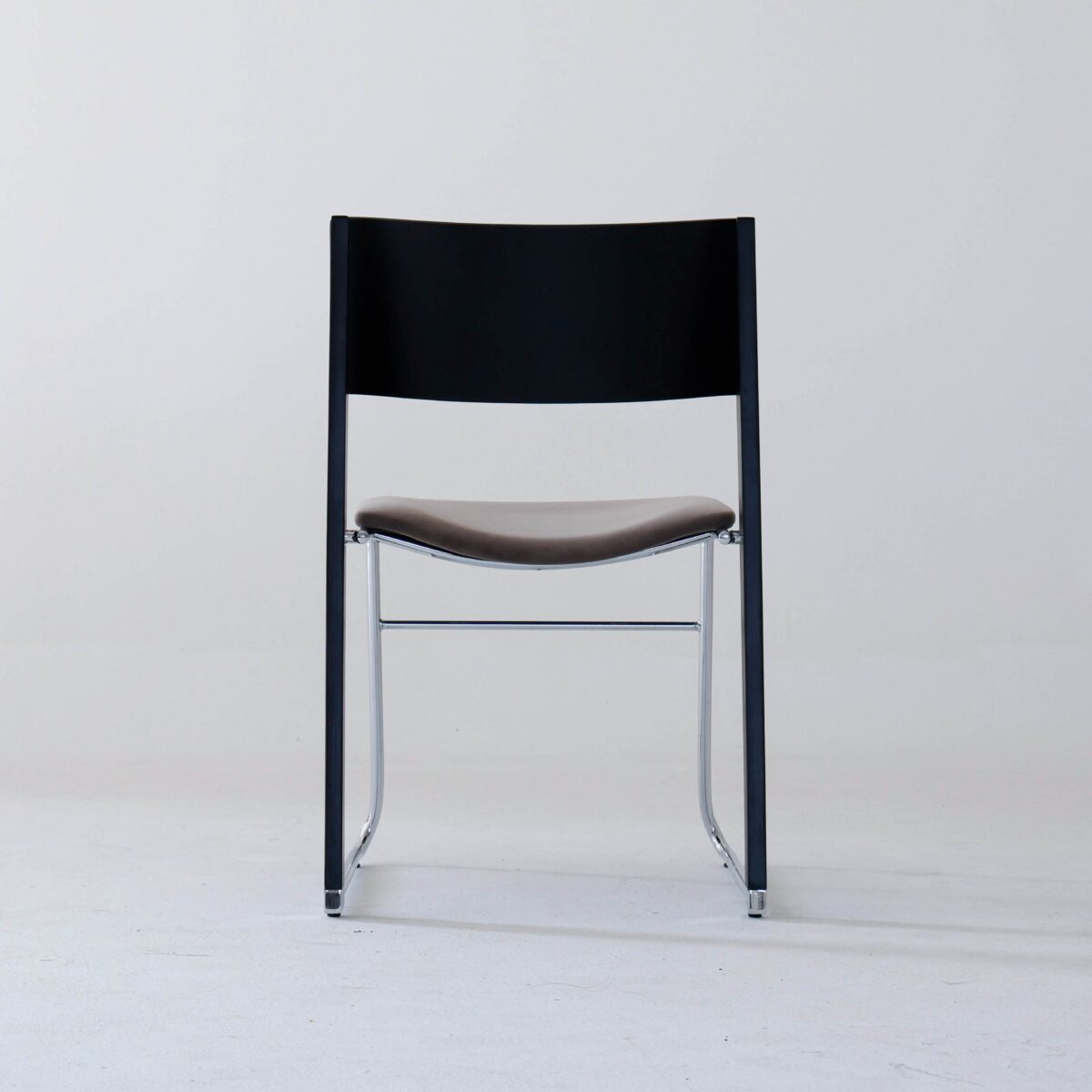 Walk Slowly Chair_Gray_B1 A minimalist chair with a black backrest, dark brown seat, and slim metal legs is positioned against a plain light grey background.