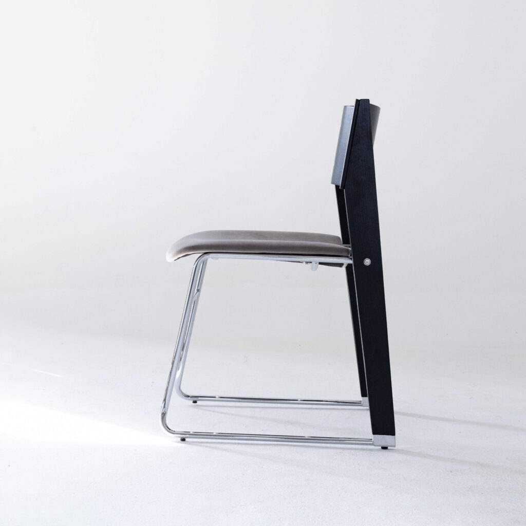 A modern chair with a sleek chrome frame, black side supports, and a padded grey seat and backrest, shown from the side on a white background.
