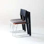 Two modern chairs with metal legs are stacked together. The front chair has a light grey cushioned seat, and the back chair has a dark backrest. Both are placed against a plain white background.