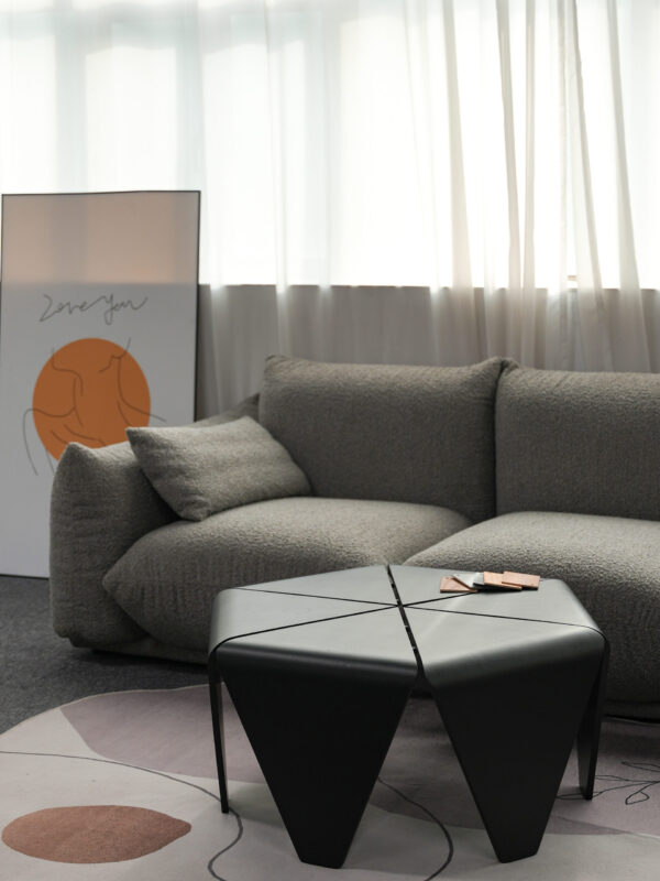 Modern living room with a textured grey sofa, black geometric metal coffee table, and an abstract art print resting against the wall, styled with soft natural light through sheer curtains.