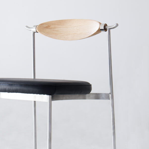 A modern chair with a black cushioned seat, slim metal frame, and a curved wooden backrest, set against a plain light background.