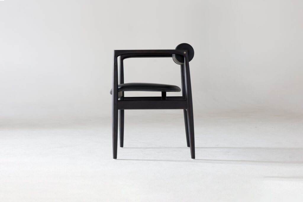 A modern black chair with a minimalist design, curved armrests, and a circular backrest detail, placed on a light grey surface against a plain white background.