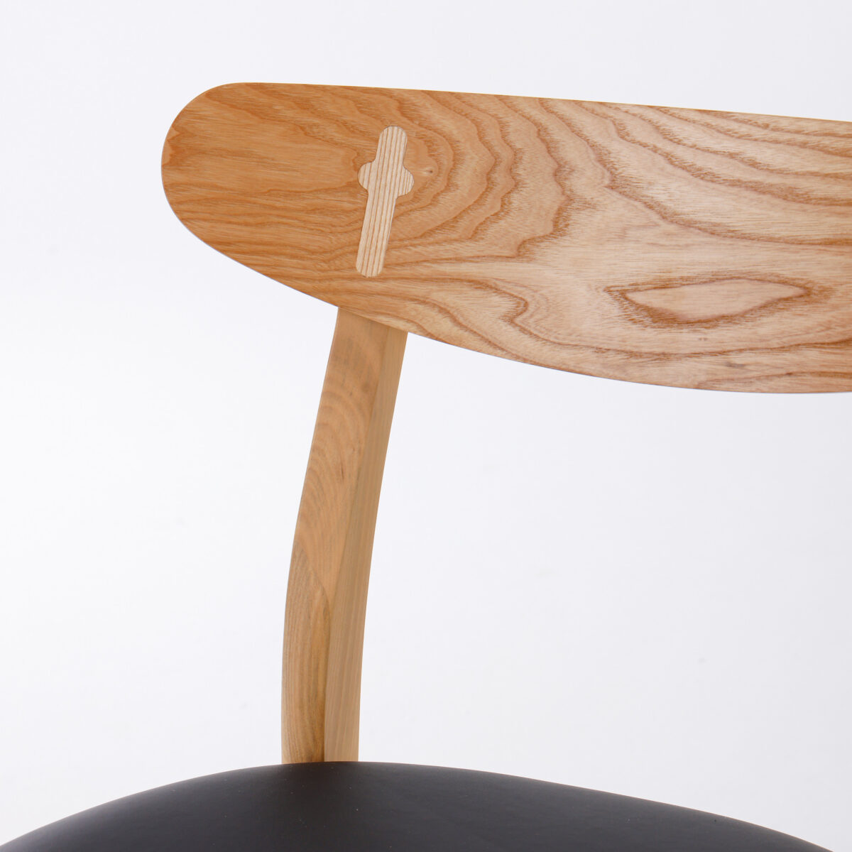 CH30P Chair_B10 A close-up of a wooden chair backrest with a natural wood grain pattern, curved design, and a black cushioned seat partially visible at the bottom. The background is plain white.