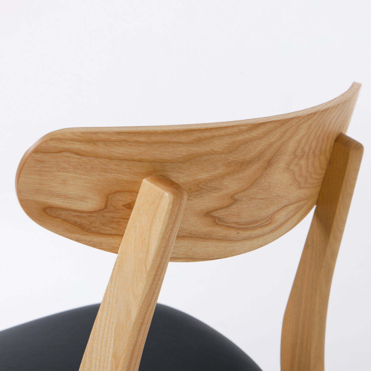 CH30P Chair_B19 Close-up of the backrest and rear legs of a wooden chair with a natural finish and visible wood grain, featuring a black seat cushion. The background is plain white.