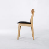 A wooden chair with a light-coloured frame, a slightly curved backrest, and a black cushioned seat, shown in profile against a plain white background.