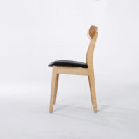 A wooden chair with a light-coloured frame, a slightly curved backrest, and a black cushioned seat, shown in profile against a plain white background.