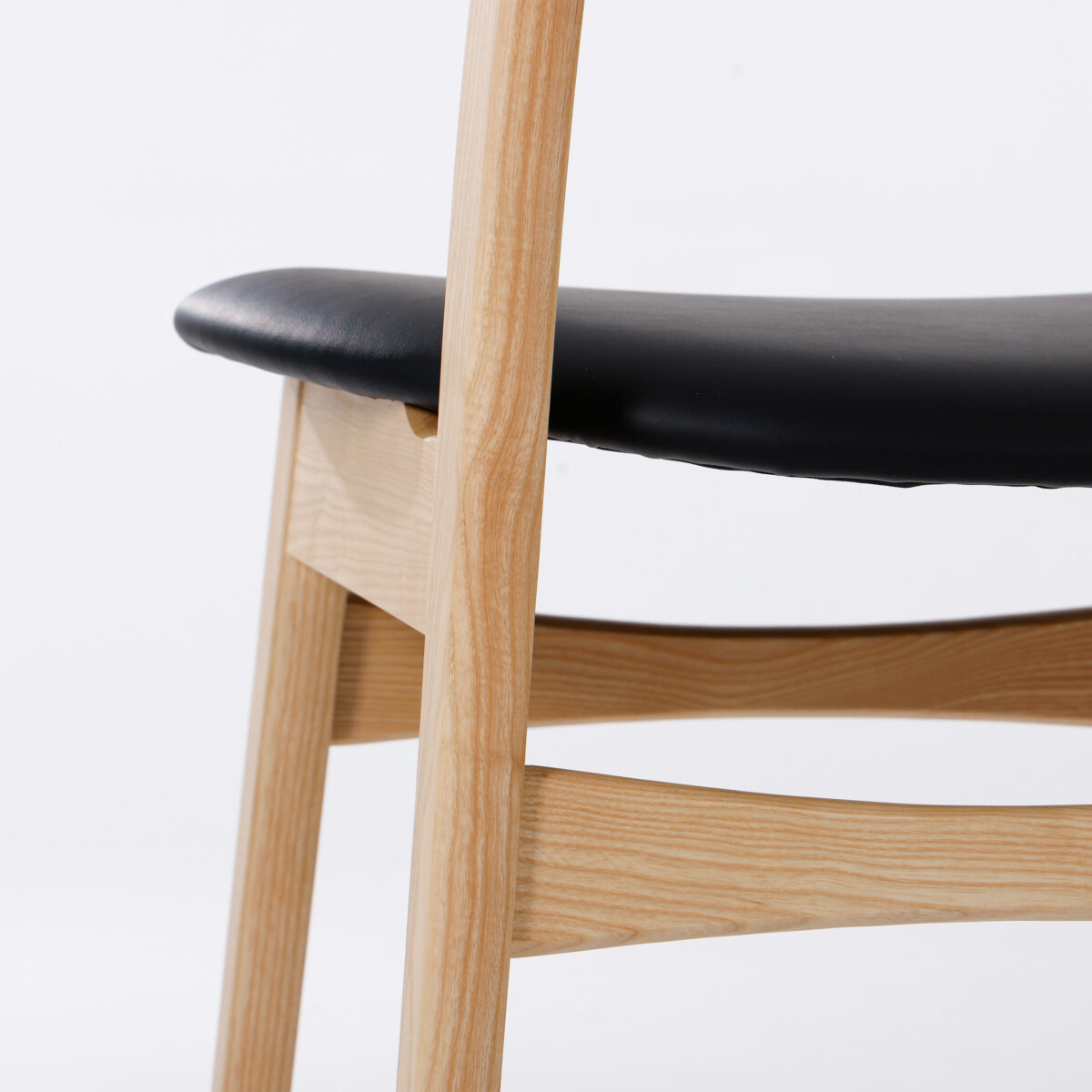 CH30P Chair_B28 Close-up of a modern wooden chair with light wood legs and frame, featuring a black cushioned seat. The background is plain white.