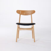 A wooden chair with a curved backrest and light wood finish, featuring a black upholstered seat, set against a plain white background.