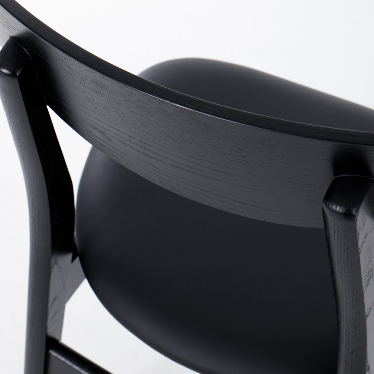 CH30P Chair_Black_B25 Close-up of the back and seat of a modern black wooden chair with a smooth, curved backrest and a padded seat, photographed against a white background.