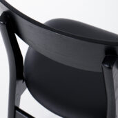 Close-up of the back and seat of a modern black wooden chair with a smooth, curved backrest and a padded seat, photographed against a white background.