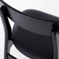 Close-up of the back and seat of a modern black wooden chair with a smooth, curved backrest and a padded seat, photographed against a white background.
