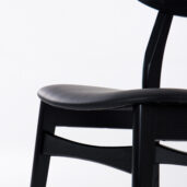 Close-up of a modern black wooden chair with a curved seat and backrest, photographed against a plain white background.