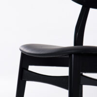 Close-up of a modern black wooden chair with a curved seat and backrest, photographed against a plain white background.